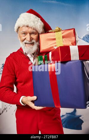 stylish handsome Santa with presents in hands with snowy mountain backdrop, winter concept Stock Photo