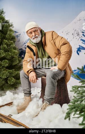 serious man with white beard in jacket sitting on tree stump looking at camera, winter concept Stock Photo