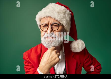 serious man dressed as Santa looking straight at camera with hand under chin, winter concept Stock Photo