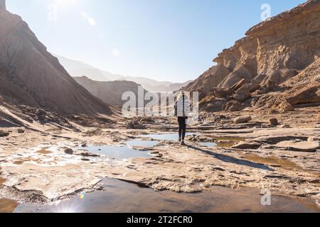 A young woman walking along the water in the desert on a trek on the Rambla Las Salinas in the desert of Tabernas, Almeria province, Andalusia Stock Photo