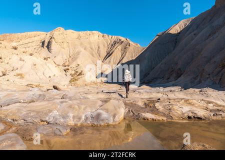 A young woman walking along the water in the desert on a trek in the Travertino waterfall and Rambla de Otero in the desert of Tabernas, Almeria Stock Photo