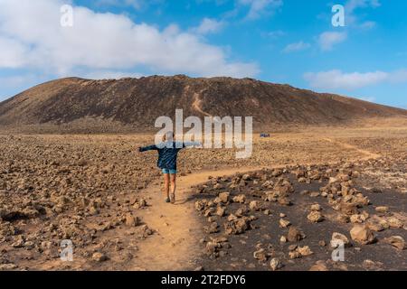 A young woman walking on the path to the Crater of the Calderon Hondo volcano near Corralejo, north coast of the island of Fuerteventura, Canary Stock Photo