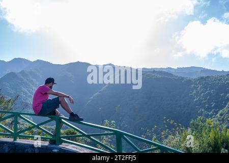 A young man sitting looking at the views from the viewpoint of the Cubo de la Galga natural park on the northeast coast on the island of La Palma Stock Photo