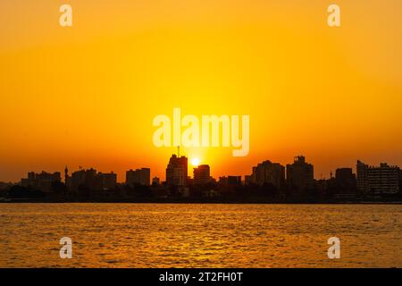 Orange sunset on the Nile river, the sun hides in the buildings of the city of Cairo in the background. Africa Stock Photo