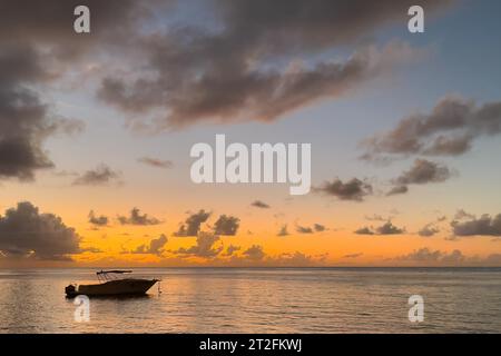 Small motorboat anchored in calm sea in safe bay during sunset with coloured sky and clouds, Pereybere, Mauritius Stock Photo