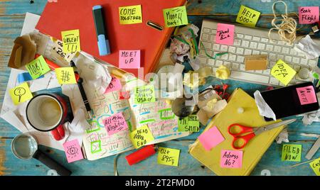 Messy workplace,chaotic office, overworked, bureaucracy,red tape concept with grungy desk,sticky notes and  various office supplies, chaotic mess. Stock Photo