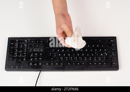 Cleaning computer keyboard in office with a wet wipe rag, dusty and dirty electronic, housework Stock Photo