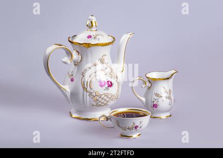 Ancient German faience tea (coffee) service with a kettle, a milk cup and a cup filled with tea (coffee) on a gray-gray background Stock Photo