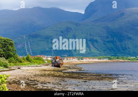 A wrecked fishing boat on the shore of Loch Linnhe, the village of Caol and Ben Nevis behind, from Corpach on the Caledonian Canal, west Scotland Stock Photo