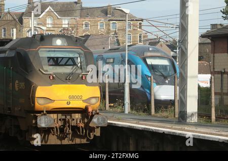 DRS class 68 diesel electric loco, 68002 Intrepid, in Carnforth station with TransPennine Express Nova 2 emu passing on the WCML, 18th October 2023. Stock Photo