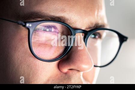 Glasses and eye. Looking at screen. Focus on work. Computer, laptop, phone or tv reflect. Tired squinting eyes. Serious man with poor eyesight. Stock Photo