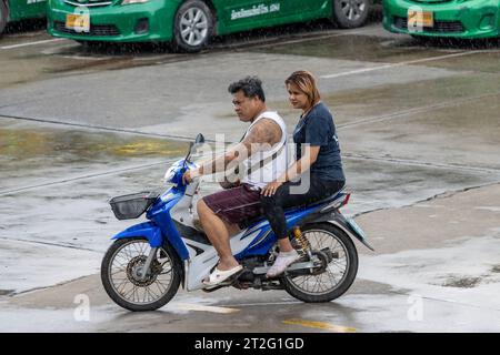 SAMUT PRAKAN, THAILAND, OCT 03 2023, A couple rides a motorcycle on the rainy street Stock Photo