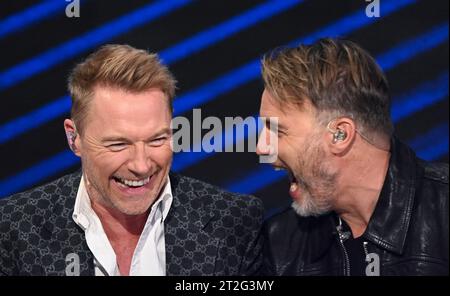 Leipzig, Germany. 18th Oct, 2023. Irish singer Ronan Keating (l) and Gary Barlow from the British pop group Take That laugh together in the 'Your Songs' show in Leipzig. Mitteldeutscher Rundfunk recorded the music show with big names. The artists perform their big hits alongside new songs in a live atmosphere, accompanied by a studio band and the 40-piece MDR Symphony Orchestra. On December 15, 'Your Songs' will be broadcast on the German public broadcaster Ersten and will be available in advance in the Mediathek from December 8. Credit: Hendrik Schmidt/dpa/Alamy Live News Stock Photo