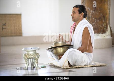 Hindu monk sitting on the floor at the Uttar Kamalabari Hindu monastery, praying and playing on cymbals, Majuli Island, India Stock Photo