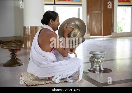 Hindu monk sitting on the floor at the Uttar Kamalabari Hindu monastery, praying and playing on cymbals, Majuli Island, India Stock Photo