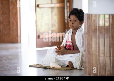 Young hindu monk in traditional clothes sitting on the floor at the Uttar Kamalabari Hindu monastery, Majuli Island, Assam, India Stock Photo