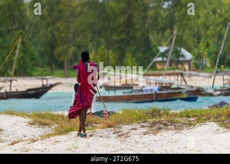 View from behind of a Zanzibar Masai dressed in traditional clothing as he stands looking at the sea at sunny day, zanzibar , Tanzania Stock Photo