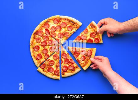Above view with a sliced pepperoni pizza and two hands grabbing slices of pizza Stock Photo