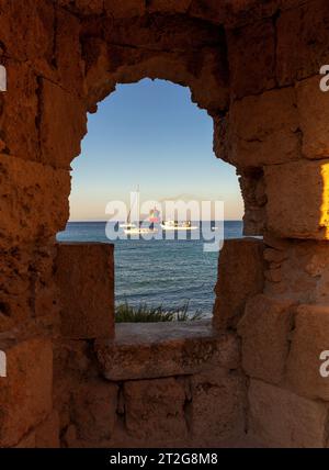 Sea view of yachts and fishing boats through the old stone fortress wall on the island of Rhodes. Greece. Stock Photo