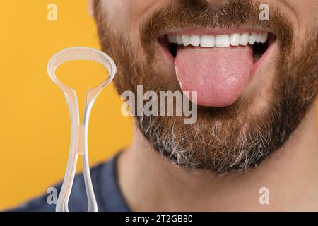 Man with tongue cleaner on yellow background, closeup Stock Photo