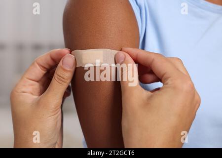 Doctor putting adhesive bandage on young woman's arm after vaccination indoors, closeup Stock Photo