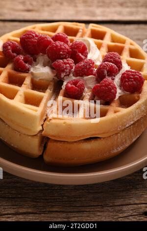 Tasty Belgian waffles with fresh raspberries and whipped cream on wooden table, closeup Stock Photo
