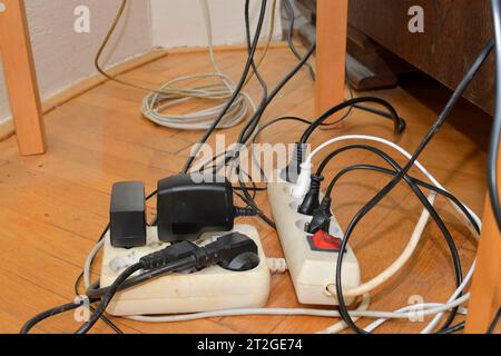 Tangled cables in the extension cord. Messy cables. Cables tangled on parquet flooring. Stock Photo