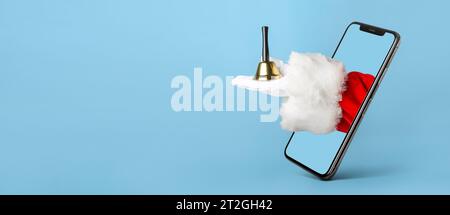 Mobile phone and hand of Santa Claus with Christmas bell on light blue background with space for text Stock Photo
