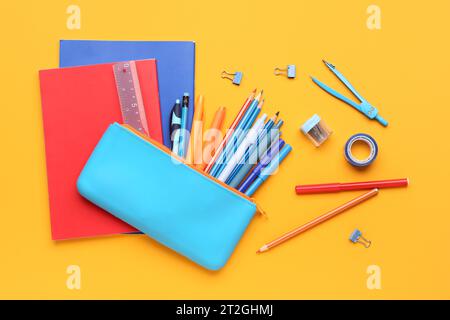 Pencil case with different stationery and notebooks on orange background Stock Photo