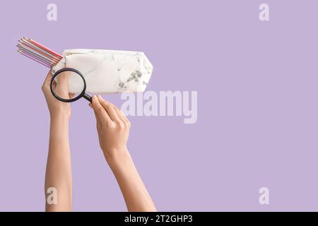 Female hands holding pencil case and magnifying glass on lilac background Stock Photo