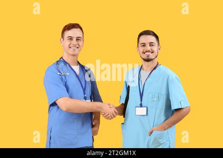 Male medical students shaking hands on yellow background Stock Photo