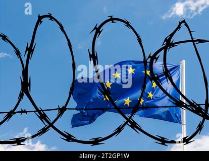 European Union EU flag against a blue sky superimposed with barbed wire relating to potentially a closed off bloc to non-EU citizens including refugee Stock Photo