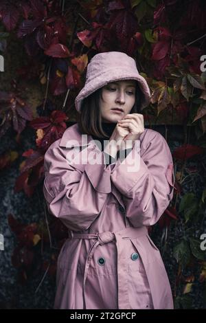 Portrait of a young woman against the backdrop of an autumn city. A model in pink clothes poses among the foliage of wild grapes Stock Photo