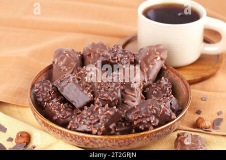 Chocolate with hazelnuts in ceramic bowl and cup of tea on the brown fabric background. Stock Photo