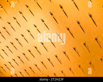 The pattern of a variety of metal forks, cutlery on the wall on a yellow background. Texture. Stock Photo