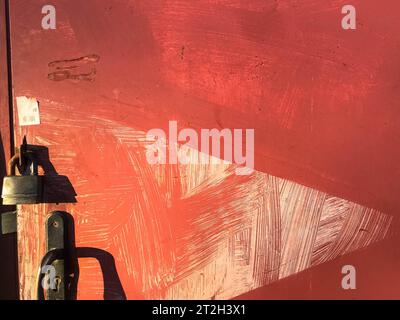 The texture of the door with a handle and a lock. Metallic iron red. Ragged, scratched. Old painted with paint with embossed lines and stains. The bac Stock Photo