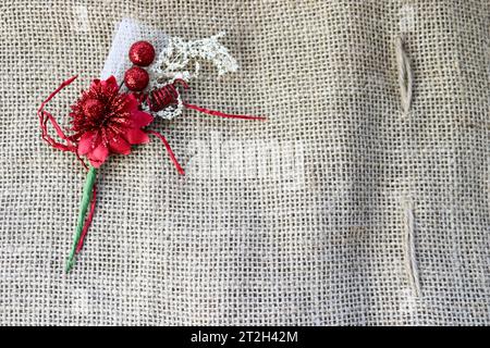A beautiful red artificial flower with a green stem on the texture of a brown old linen cloth, linen natural material with a rough perpendicular inter Stock Photo