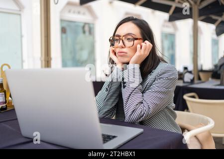 Bored inefficient woman office employee using laptop sitting at restaurant table leaning head on hands, lonely disappointed female tired of wimp work. Stock Photo