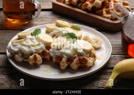 Delicious Belgian waffles with banana and whipped cream served on wooden table Stock Photo