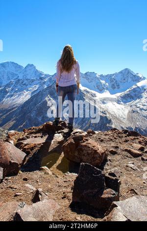 The girl with her back to the camera looking at the tall mountains in ...