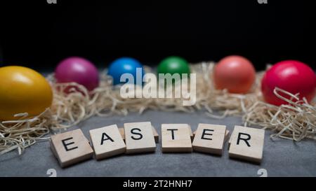 Happy Easter! The Easter eggs are colored and lying in the straw. Preparations for Easter. On the table are letters that spell out the word Easter Stock Photo