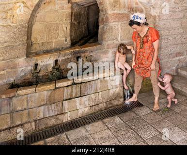 Ein Kerem, Israel - August 12, 2023: Children with their mother, playing with the water in Miriam's Well, or Miriam's Spring, called 'Fountain of the Stock Photo