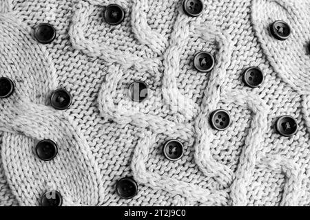 Beautiful texture of a soft warm natural sweater with a knitted pattern of yarn and black and white small round buttons. The background. Stock Photo
