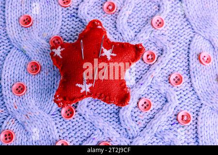 Beautiful texture of a soft warm natural sweater, knitted fabrics and red small round buttons for sewing and a needle pad. Flat lay. The background. Stock Photo
