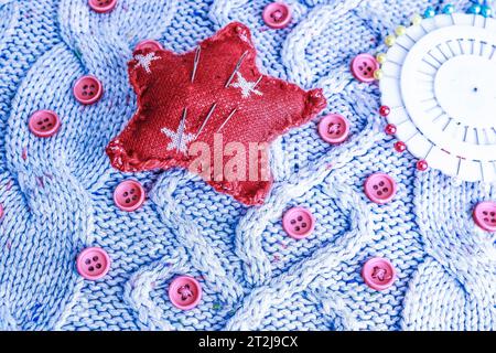 Beautiful texture of a soft warm natural sweater, knitted fabrics and red small round buttons for sewing and a needle pad. Flat lay. The background. Stock Photo