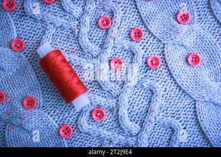 Beautiful texture of a soft warm natural sweater, fabrics with a knitted pattern of yarn and red small round buttons for sewing and a skein of red thr Stock Photo