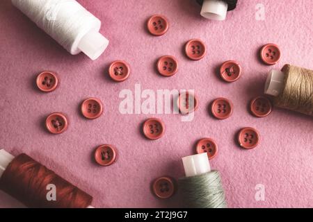 Beautiful frame with a lot of round red buttons for sewing, needlework and skeins of spools of thread. Copy space. Flat lay. Purple pink background. Stock Photo