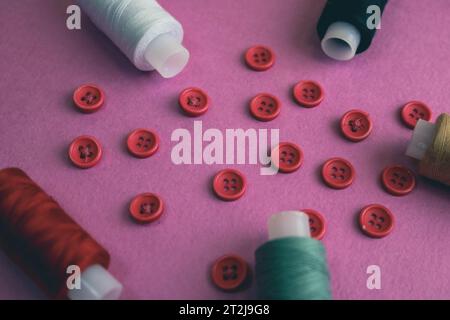 Beautiful frame with a lot of round red buttons for sewing, needlework and skeins of spools of thread. Copy space. Flat lay. Purple pink background. Stock Photo