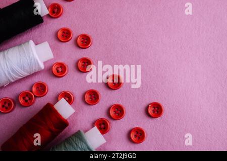 Beautiful texture with lots of round red buttons for sewing, needlework and skeins of spools of thread. Copy space. Flat lay. Pink, purple background. Stock Photo