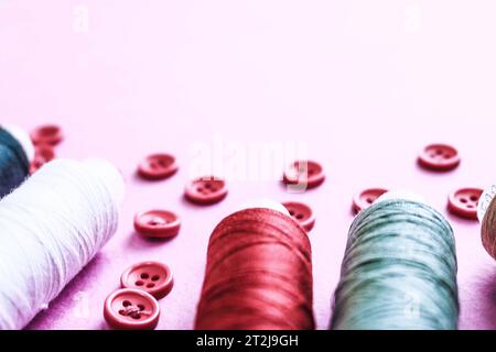 Beautiful texture with lots of round red buttons for sewing, needlework and skeins of spools of thread. Copy space. Flat lay. Pink, purple background. Stock Photo